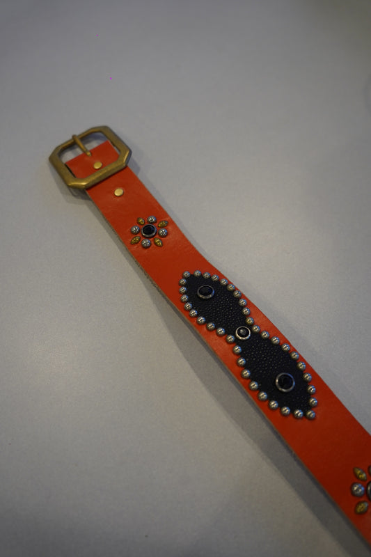 Vintage studded belt close-up showing orange leather, alternating silver pyramid stud rows and black backing