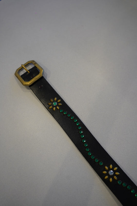 Vintage studded leather belt close-up, black hide with blue floral motif and antiqued silver buckle hardware.