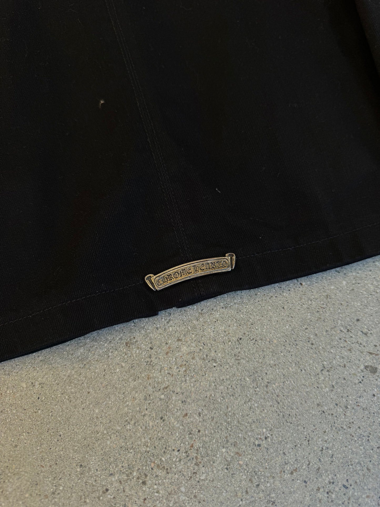 Chrome Hearts black jacket back hem detail showing engraved silver Chrome Hearts plaque tag
