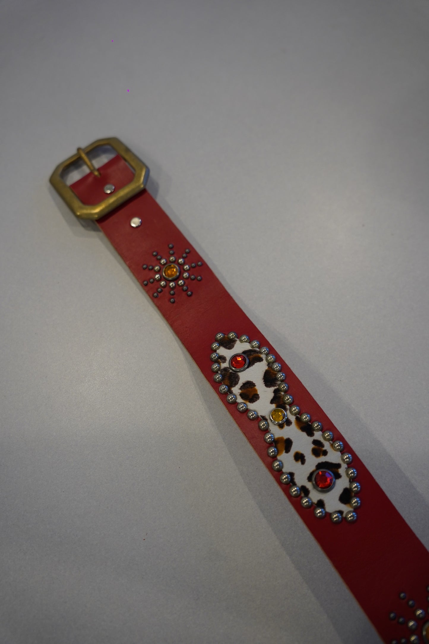 Vintage red cowhide studded belt coiled view, dense pyramid studs along strap with classic single-prong buckle.