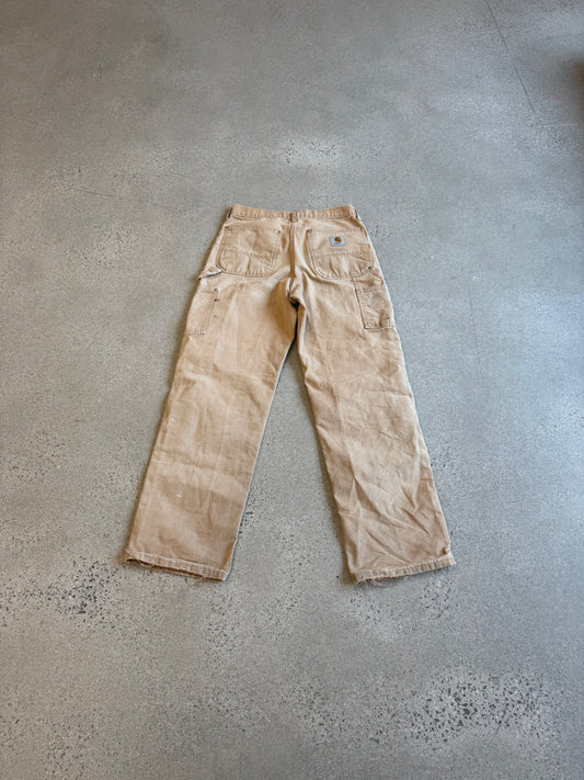 Vintage Carhartt tan carpenter pants back view with twin patch pockets and signature label, photographed on concrete.