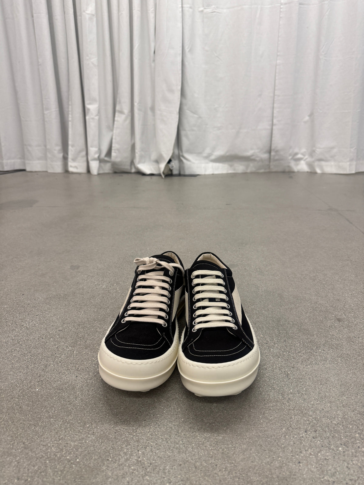Rick Owens DRKSHDW black Vintage sneakers front view on concrete floor showing white toe cap and waxed laces.
