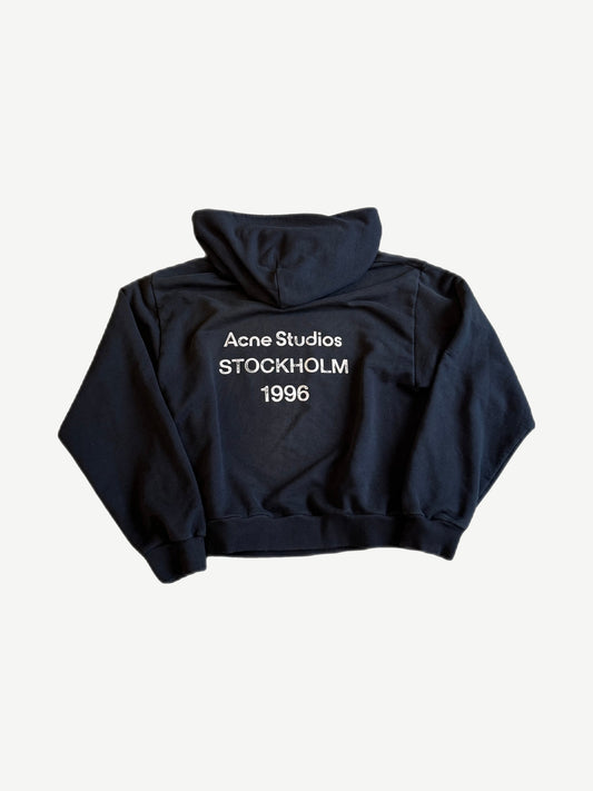 Back of Acne Studios black fleece hoodie with white Acne Studios Stockholm 1996 logo print.