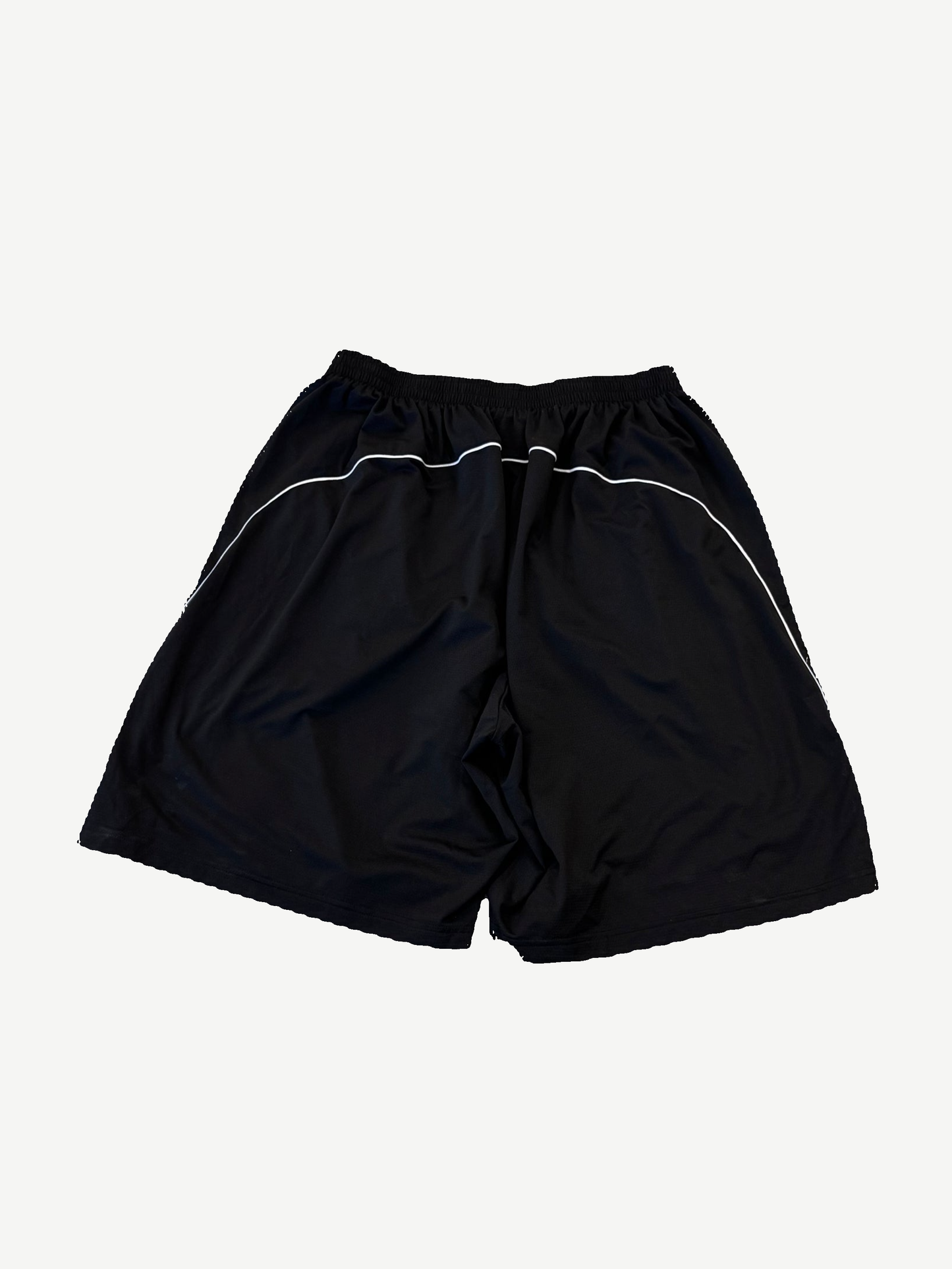 Back of Balenciaga Lamborghini black baggy shorts with white piping along seams and elastic waistband.