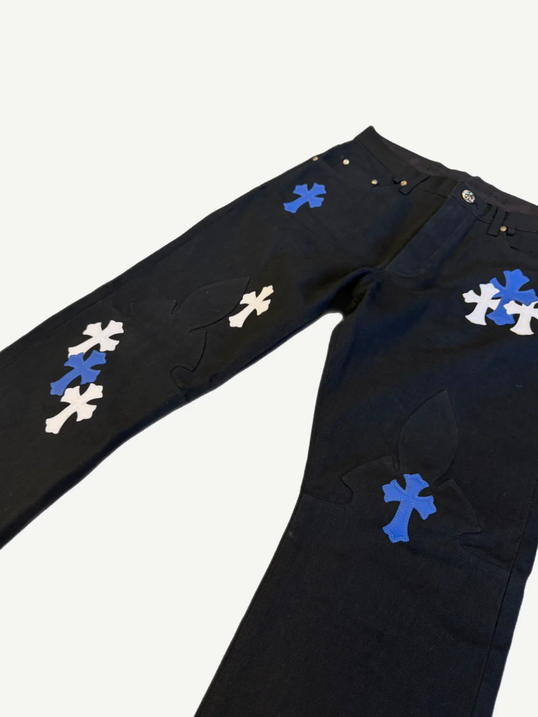 Chrome Hearts black fleur knee jeans angled detail, blue white leather cross patches clustered along leg seam.