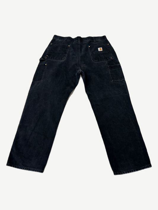 Back of vintage Carhartt black double knee carpenter pants showing Carhartt label and worn workwear fade