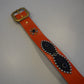 Vintage studded belt close-up showing orange leather, alternating silver pyramid stud rows and black backing