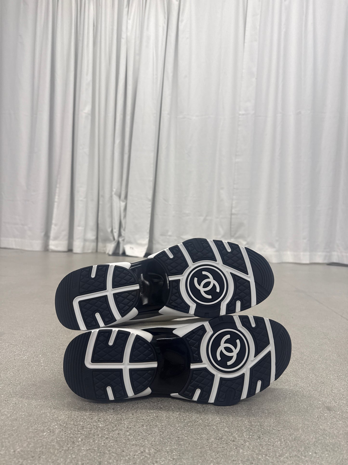 Chanel low top trainer outsole pair showing navy rubber tread with white CC circle logo on each sole