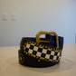 Vintage black leather belt coiled with brass studs framing checkerboard panel and brass buckle