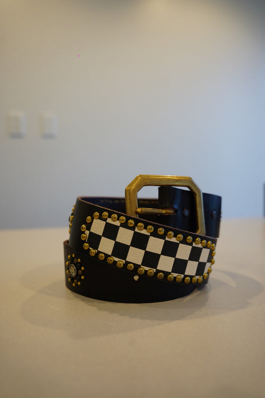 Vintage black leather belt coiled with brass studs framing checkerboard panel and brass buckle