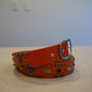 Vintage orange leather belt coiled, silver pyramid studs lining length with classic buckle