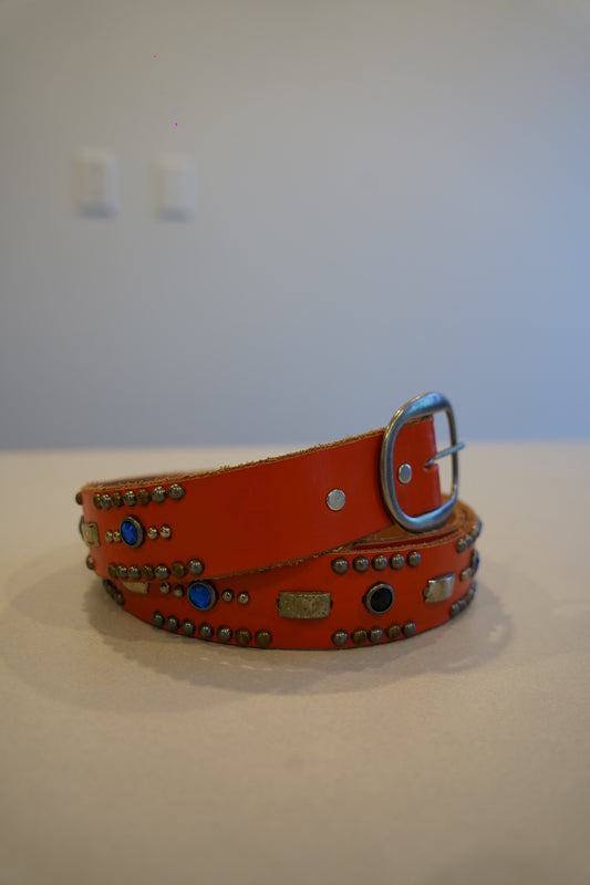 Vintage orange leather belt coiled, silver pyramid studs lining length with classic buckle