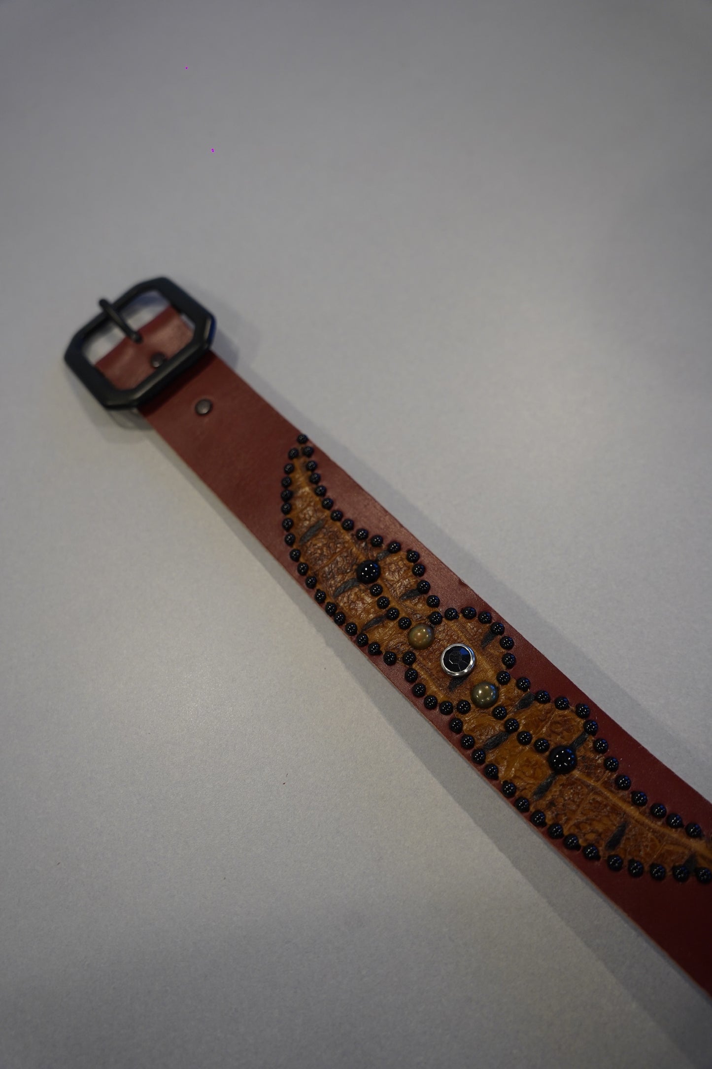 Vintage brown leather belt laid flat showing embossed spider motif, blue glass cabochons and black studs