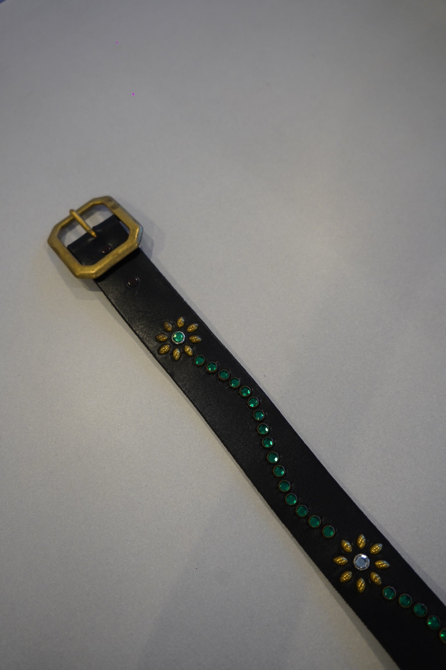 Vintage studded leather belt close-up, black hide with blue floral motif and antiqued silver buckle hardware.