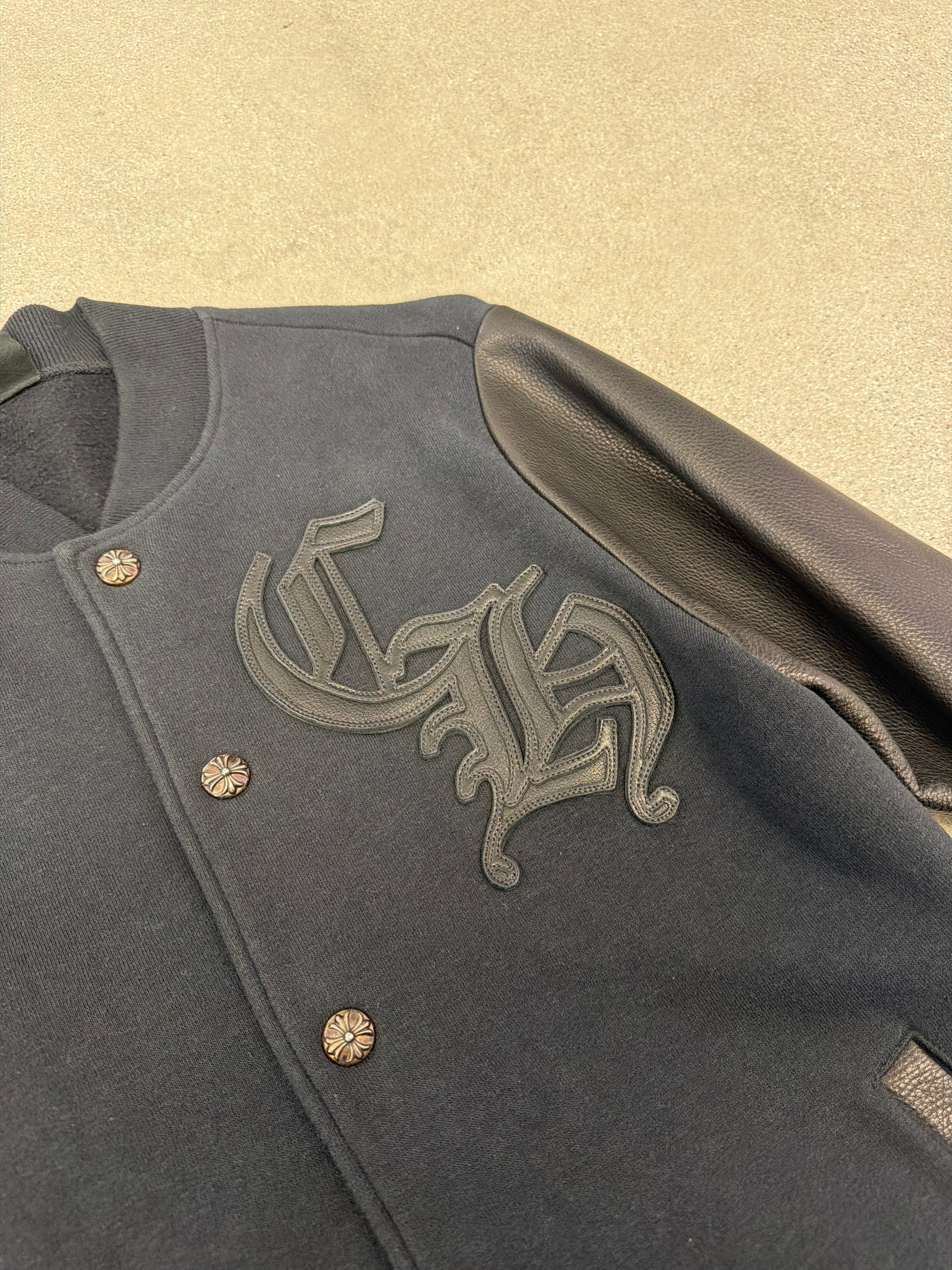 Close-up of Chrome Hearts varsity jacket CH gothic logo embroidery and silver cross button detail on navy wool