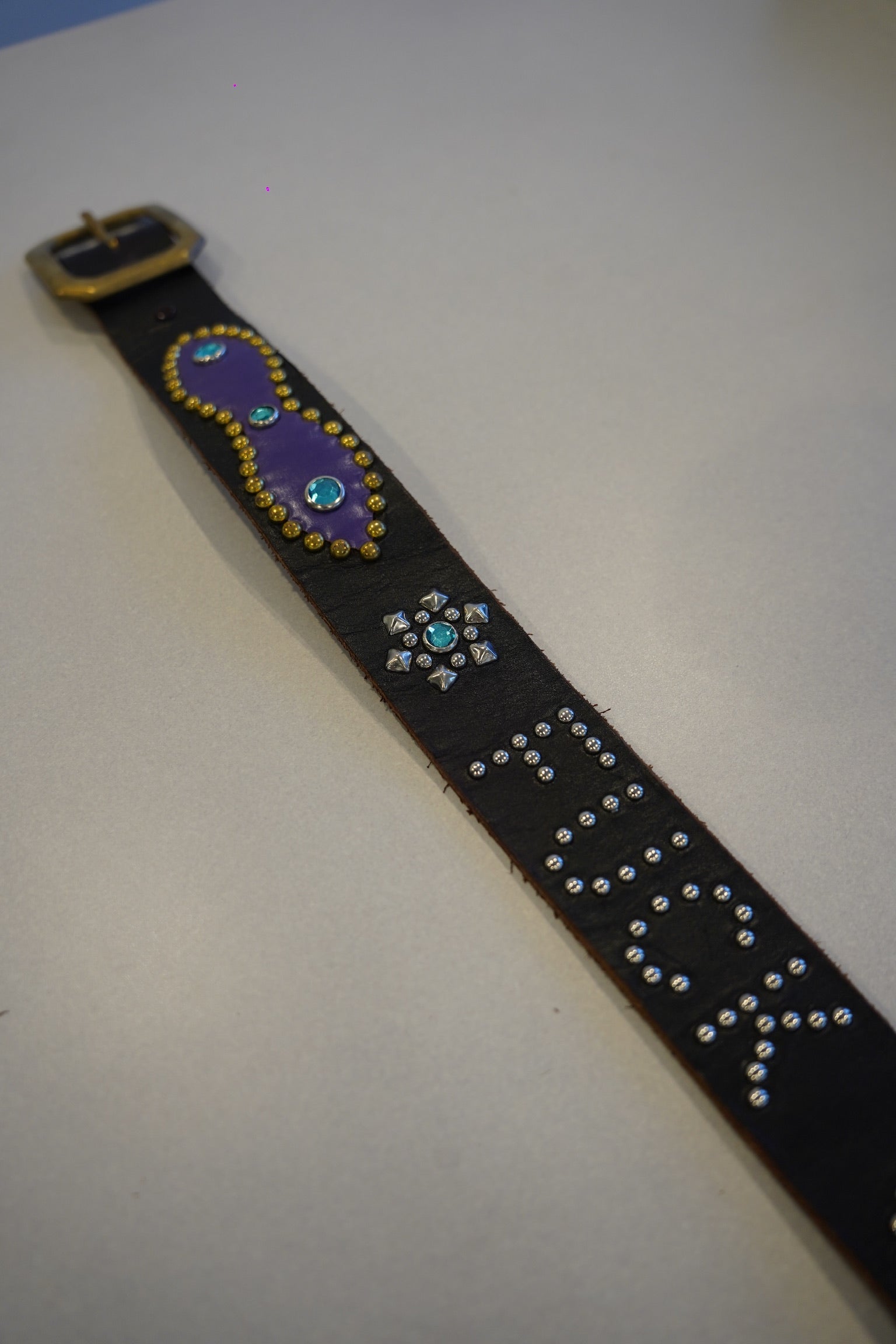 Vintage studded black belt laid flat with purple painted panel, turquoise gem star and stud-spelled text