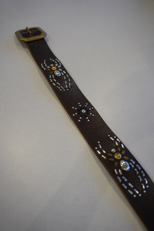 Vintage brown leather belt laid flat showing studded spider and starburst medallions along the strap