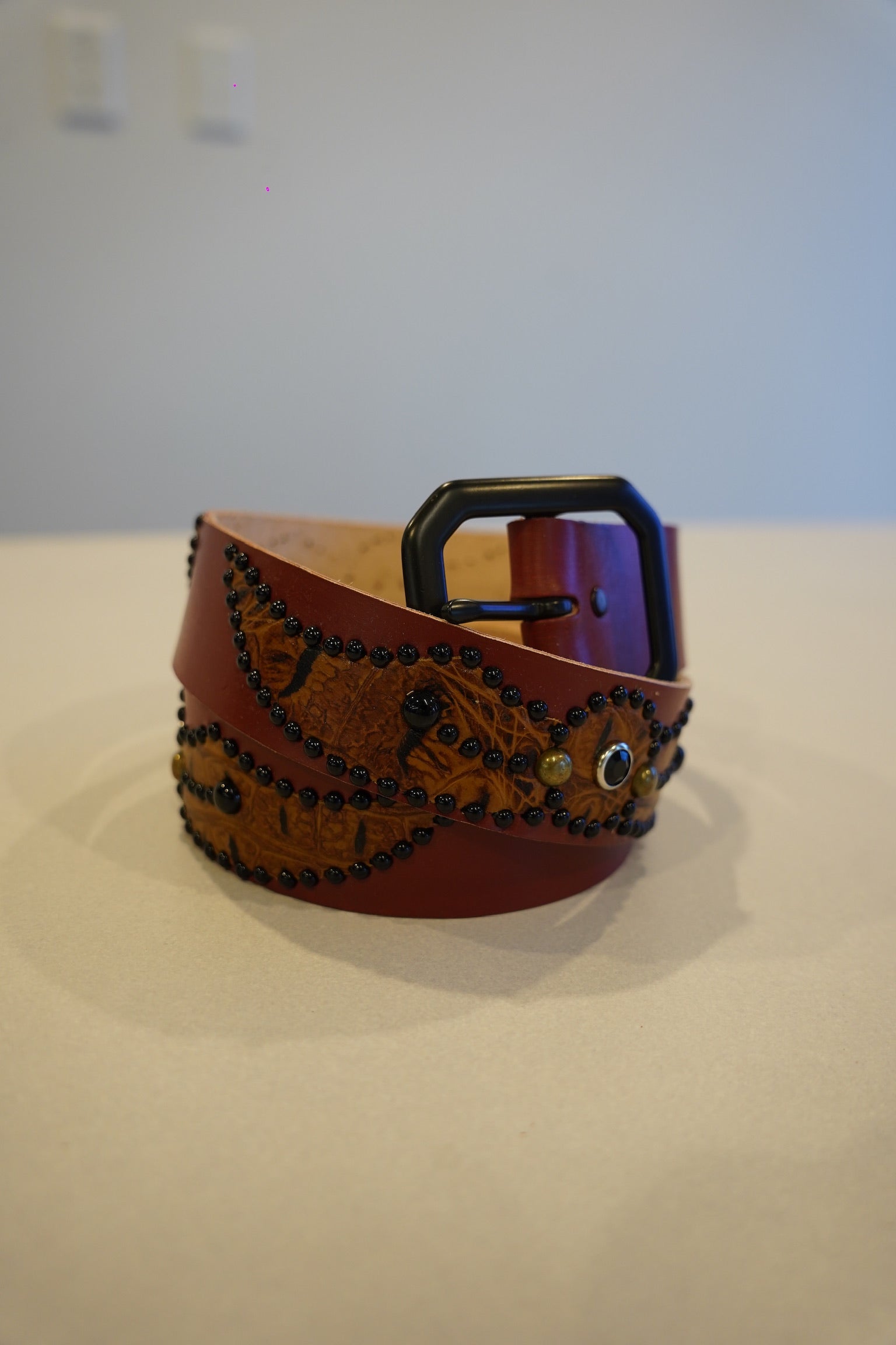 Vintage brown leather belt coiled with embossed winged-spider panel, black bead studs and matte buckle