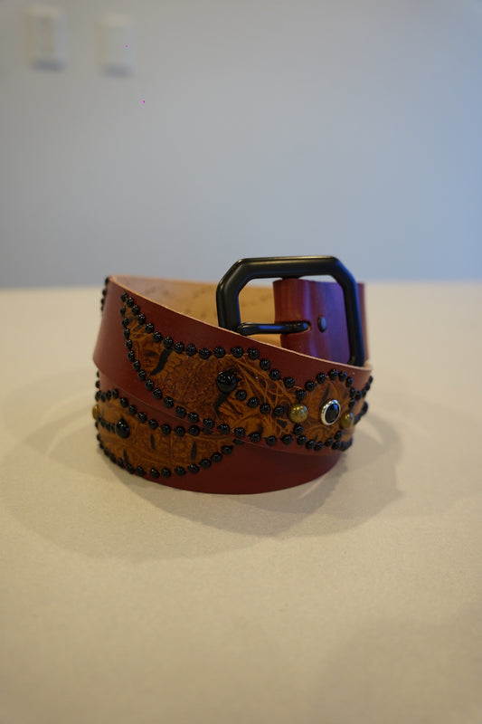 Vintage brown leather belt coiled with embossed winged-spider panel, black bead studs and matte buckle