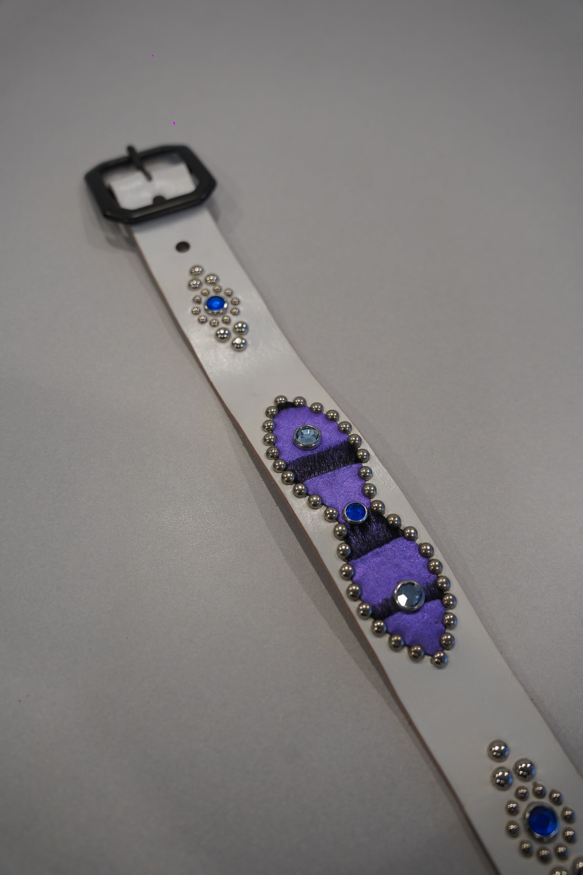 Flat view of vintage white leather belt with purple ponyhair panels, silver studs and blue gem accents