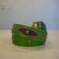Vintage green leather belt coiled with purple snakeskin inlays, silver studs, and brass buckle.