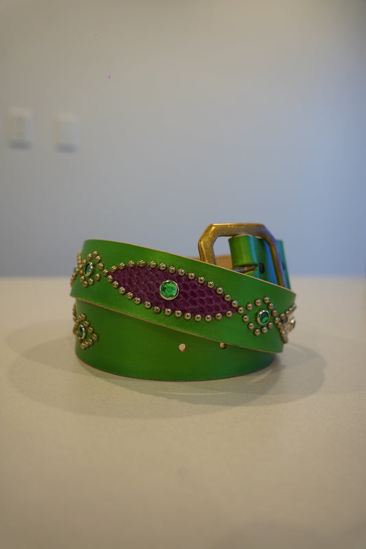 Vintage green leather belt coiled with purple snakeskin inlays, silver studs, and brass buckle.
