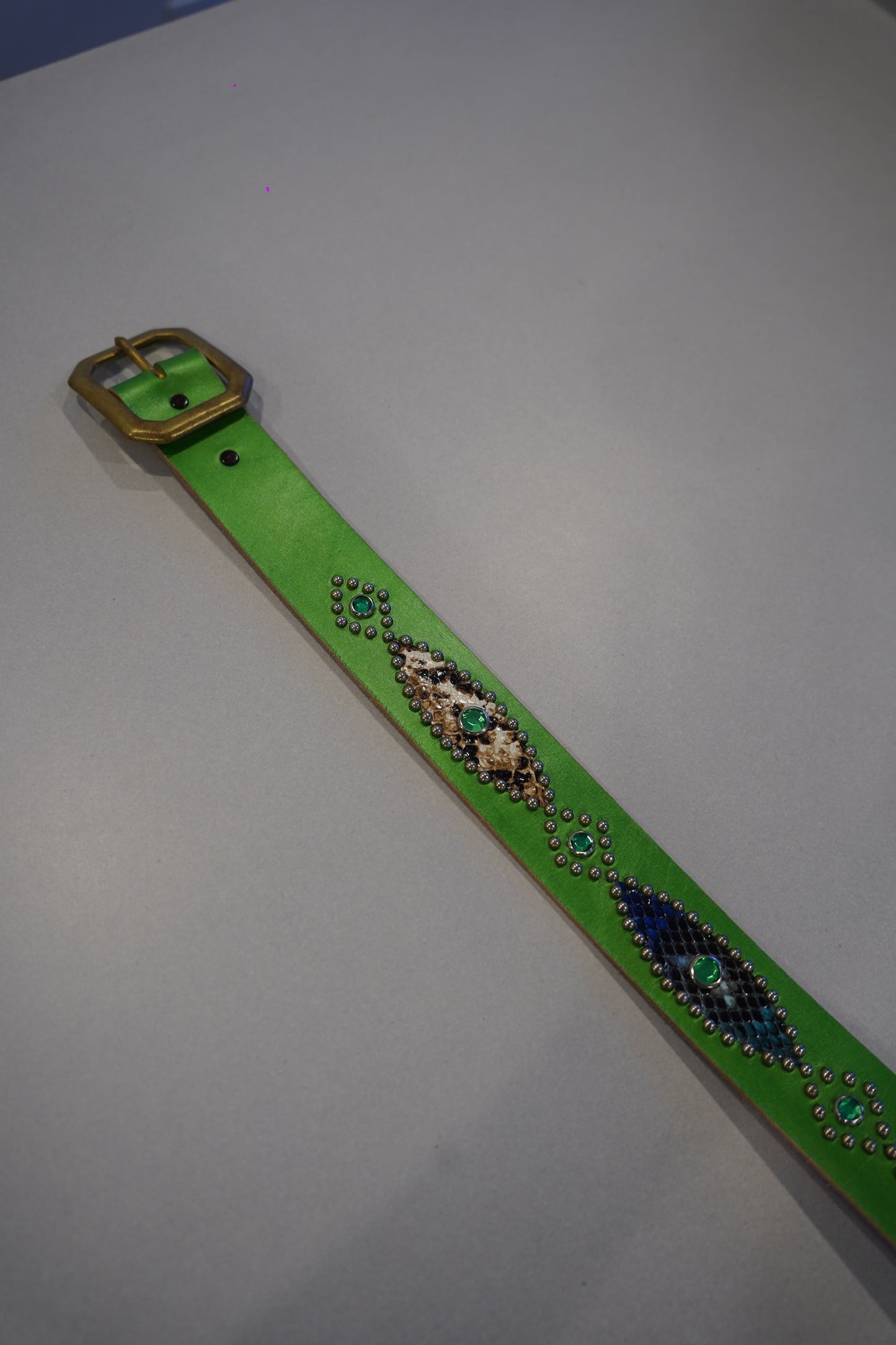 Vintage green snakeskin studded leather belt laid flat with brass square buckle and gemstone accents.