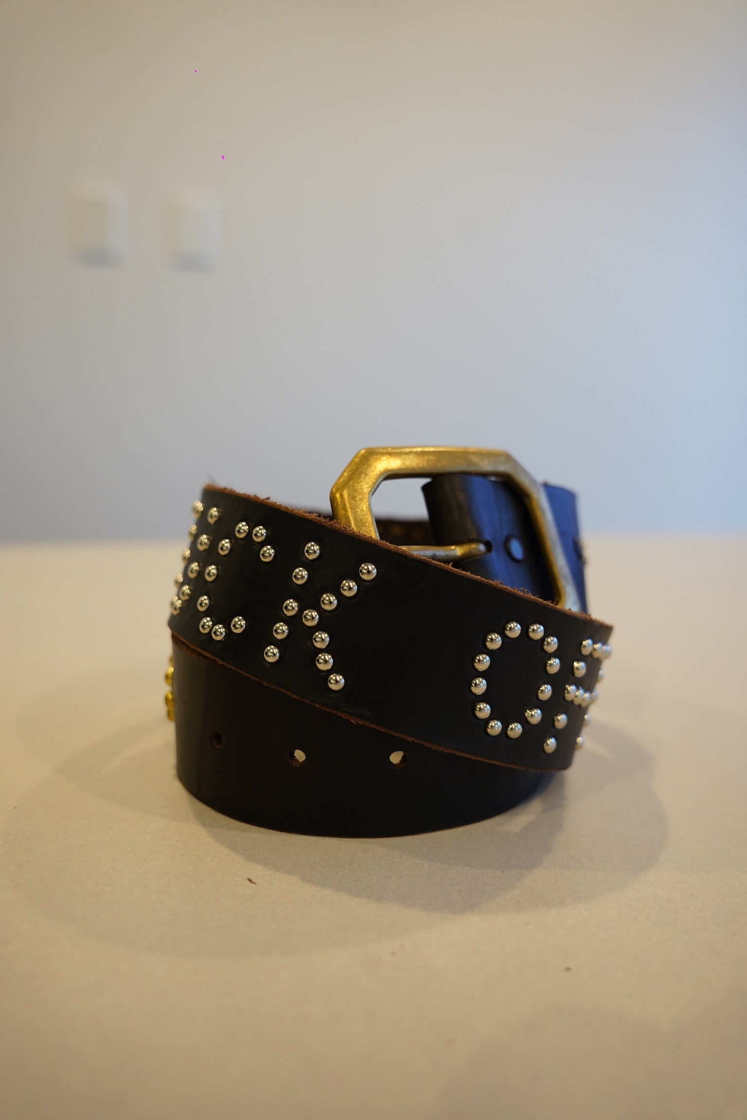 Vintage black leather studded belt coiled with brass buckle and silver stud lettering across the strap