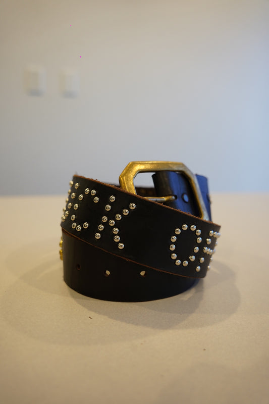 Vintage black leather studded belt coiled with brass buckle and silver stud lettering across the strap