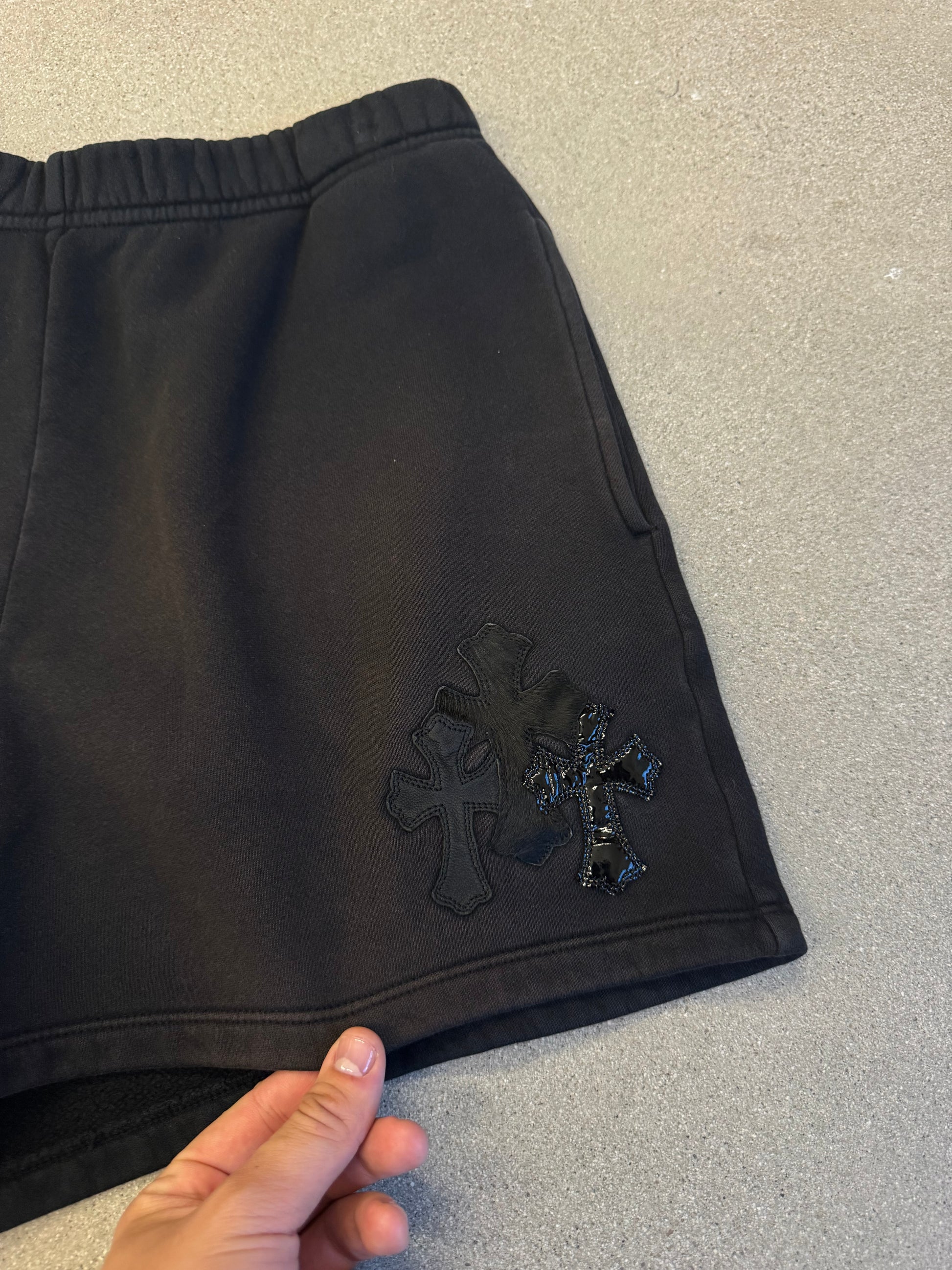 Chrome Hearts black sweat shorts close-up of layered black leather cross patches with tonal stitch detailing