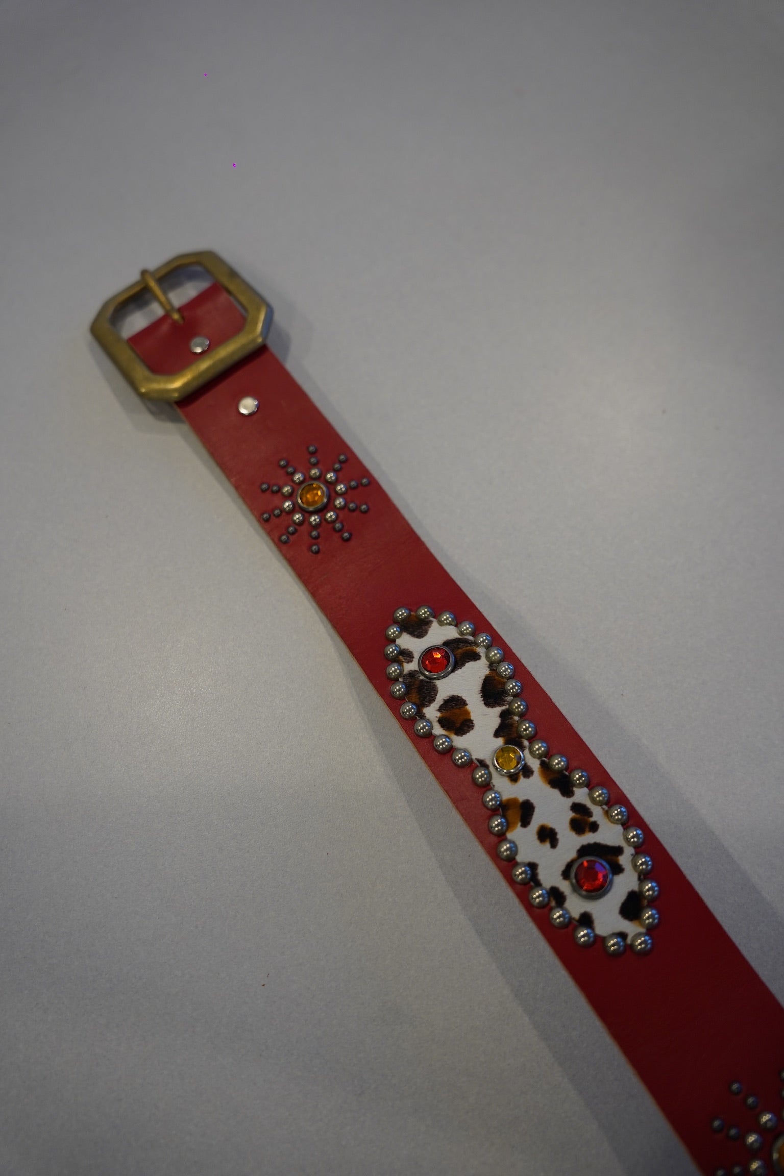 Vintage red cowhide studded belt coiled view, dense pyramid studs along strap with classic single-prong buckle.