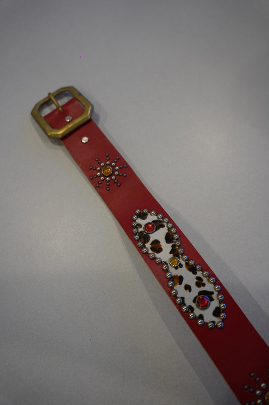 Vintage red cowhide studded belt coiled view, dense pyramid studs along strap with classic single-prong buckle.