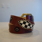 Vintage burgundy leather belt coiled with brass buckle, checkerboard studded panel and beaded rosette accents.