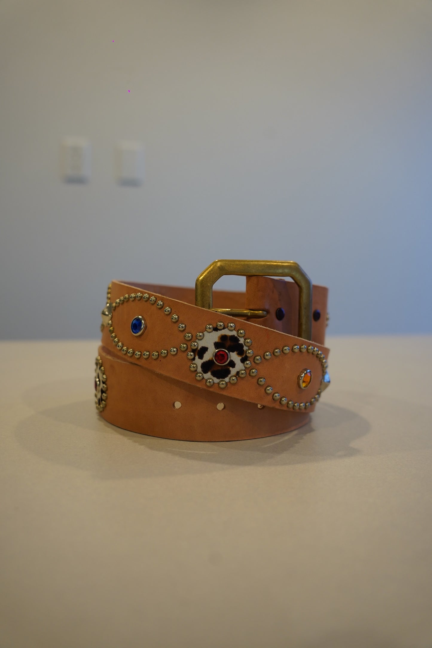 Vintage tan leather belt coiled with brass buckle, silver bead trim, leopard inlay medallions and jewel studs.
