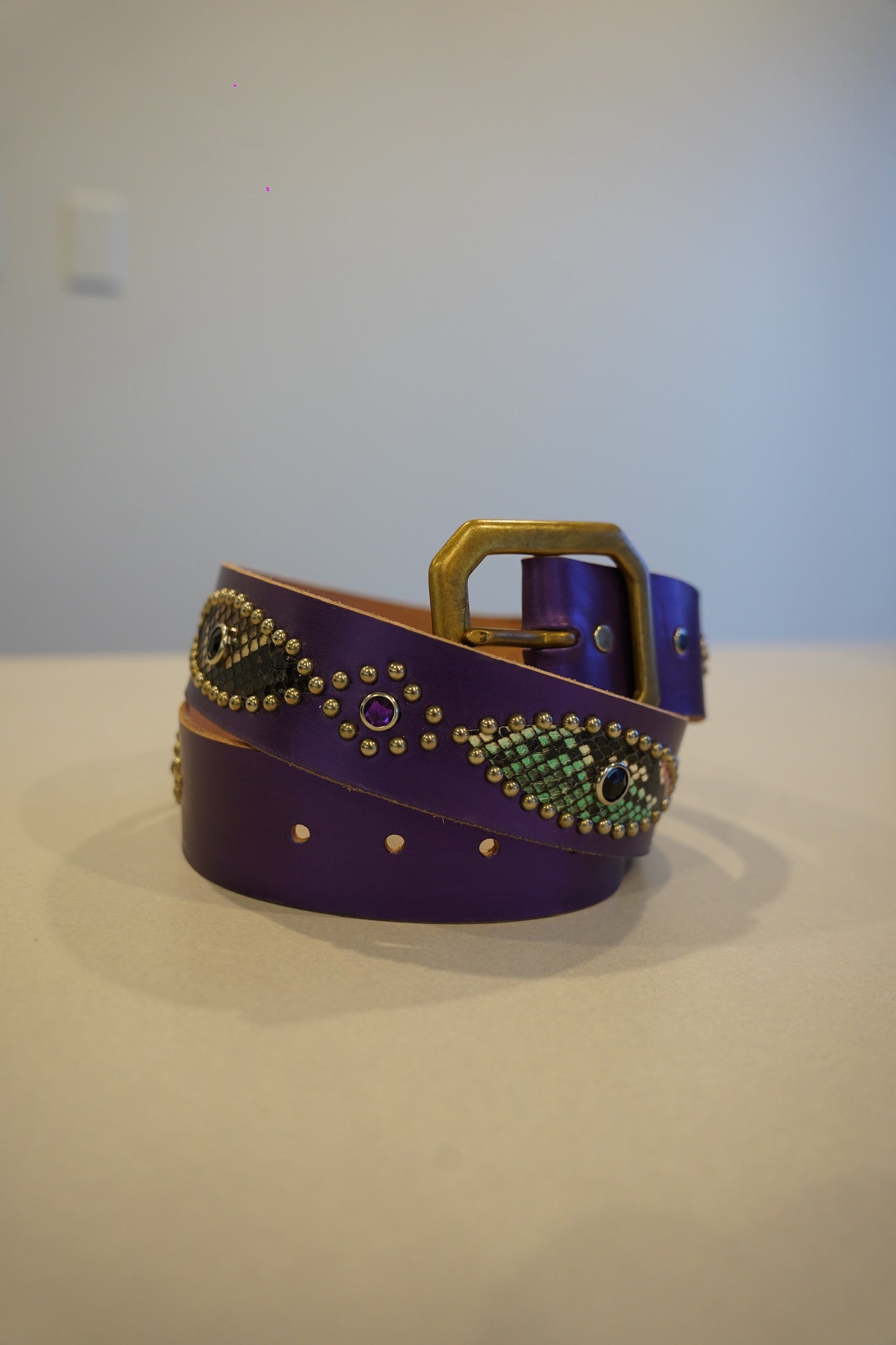 Vintage purple leather belt coiled with brass buckle, snakeskin medallion inlays and gemstone studs