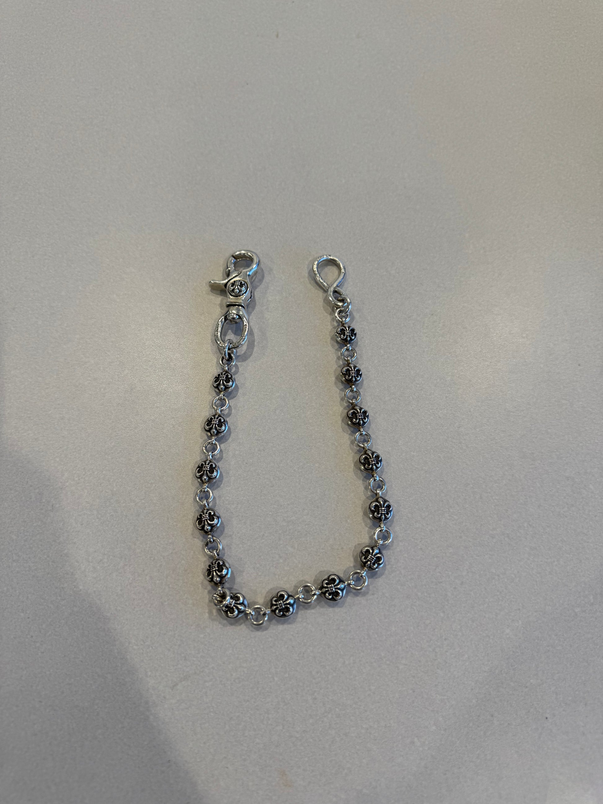 Chrome Hearts Fleur ball wallet chain draped on white surface showing silver fleur-engraved beads and hardware