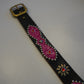 Flat view of vintage black leather belt with pink snakeskin studded medallions and brass buckle detail.