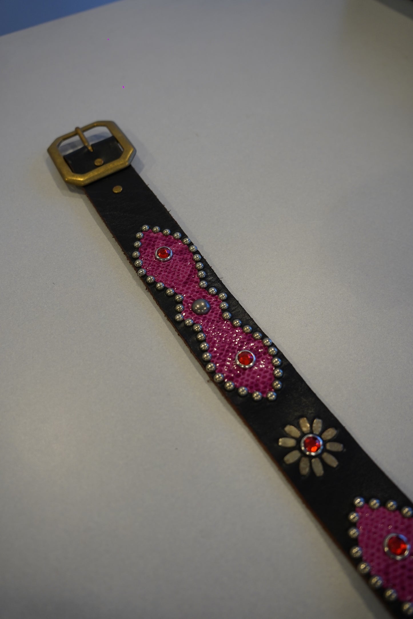 Flat view of vintage black leather belt with pink snakeskin studded medallions and brass buckle detail.