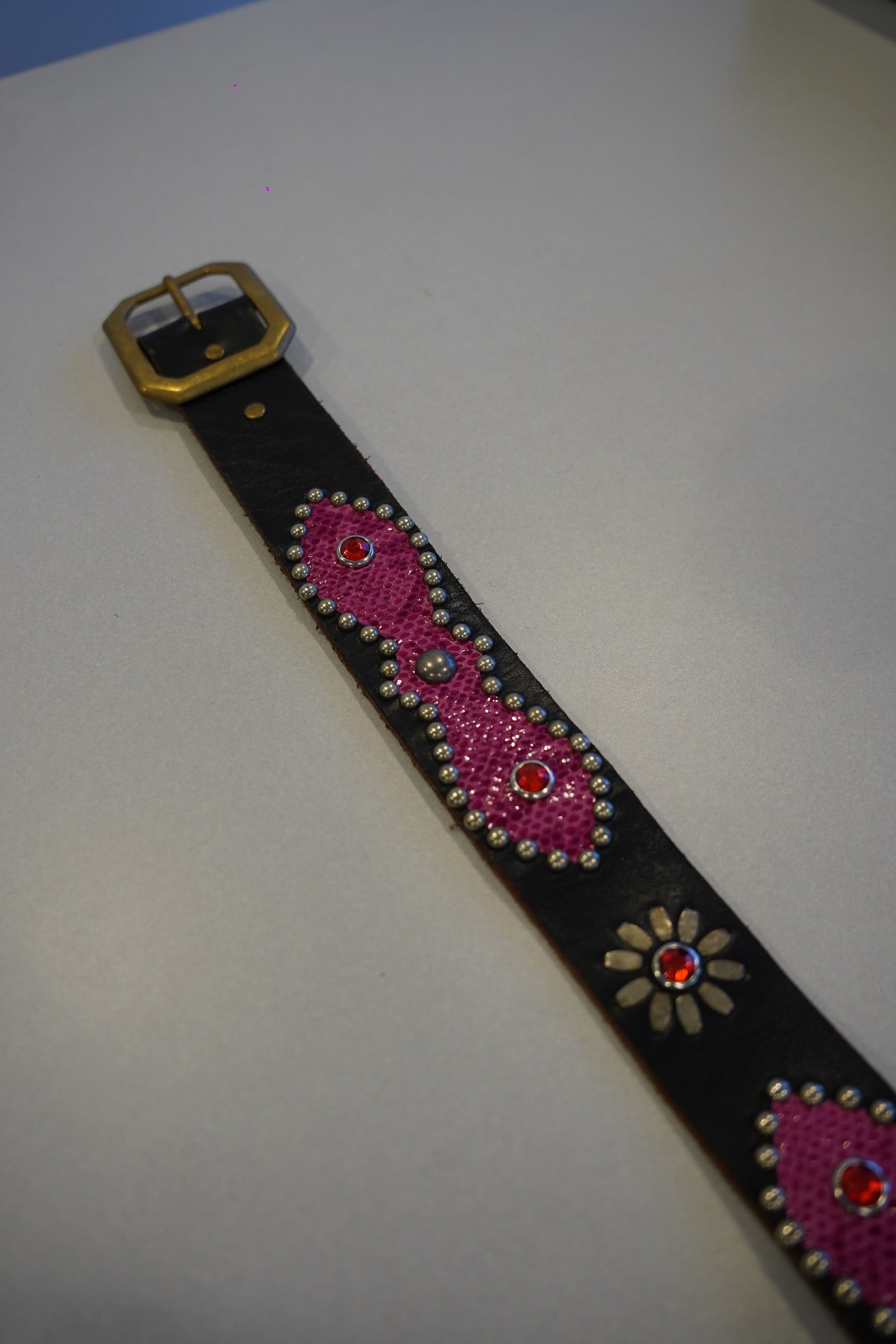 Flat view of vintage black leather belt with pink snakeskin studded medallions and brass buckle detail.