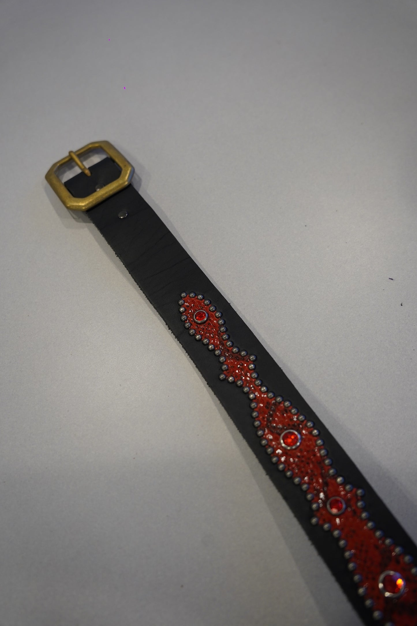Vintage studded snakeskin belt flat view with black red scale texture, metal buckle and dense stud rows