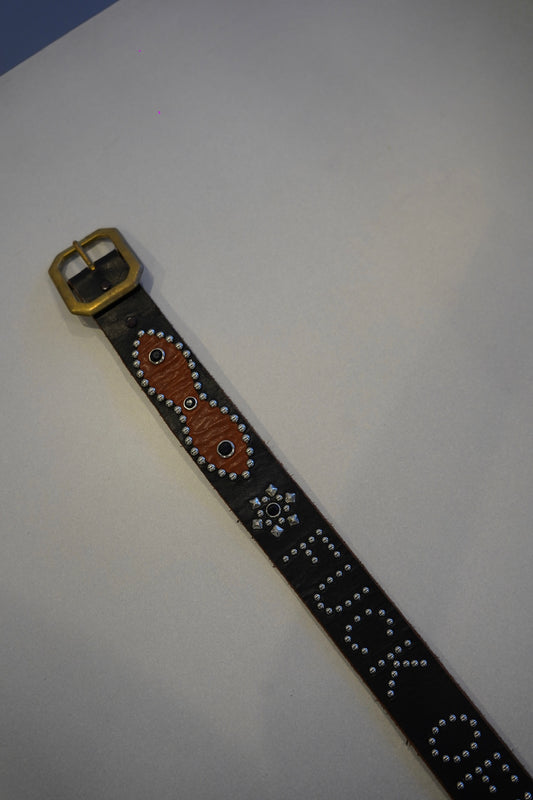 Vintage studded belt close-up showing orange Fuck Off graphic and silver pyramid studs on aged black leather