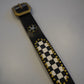 Vintage black studded leather belt laid flat showing checkerboard print and rhinestone medallion