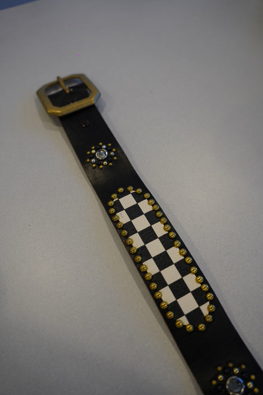 Vintage black studded leather belt laid flat showing checkerboard print and rhinestone medallion