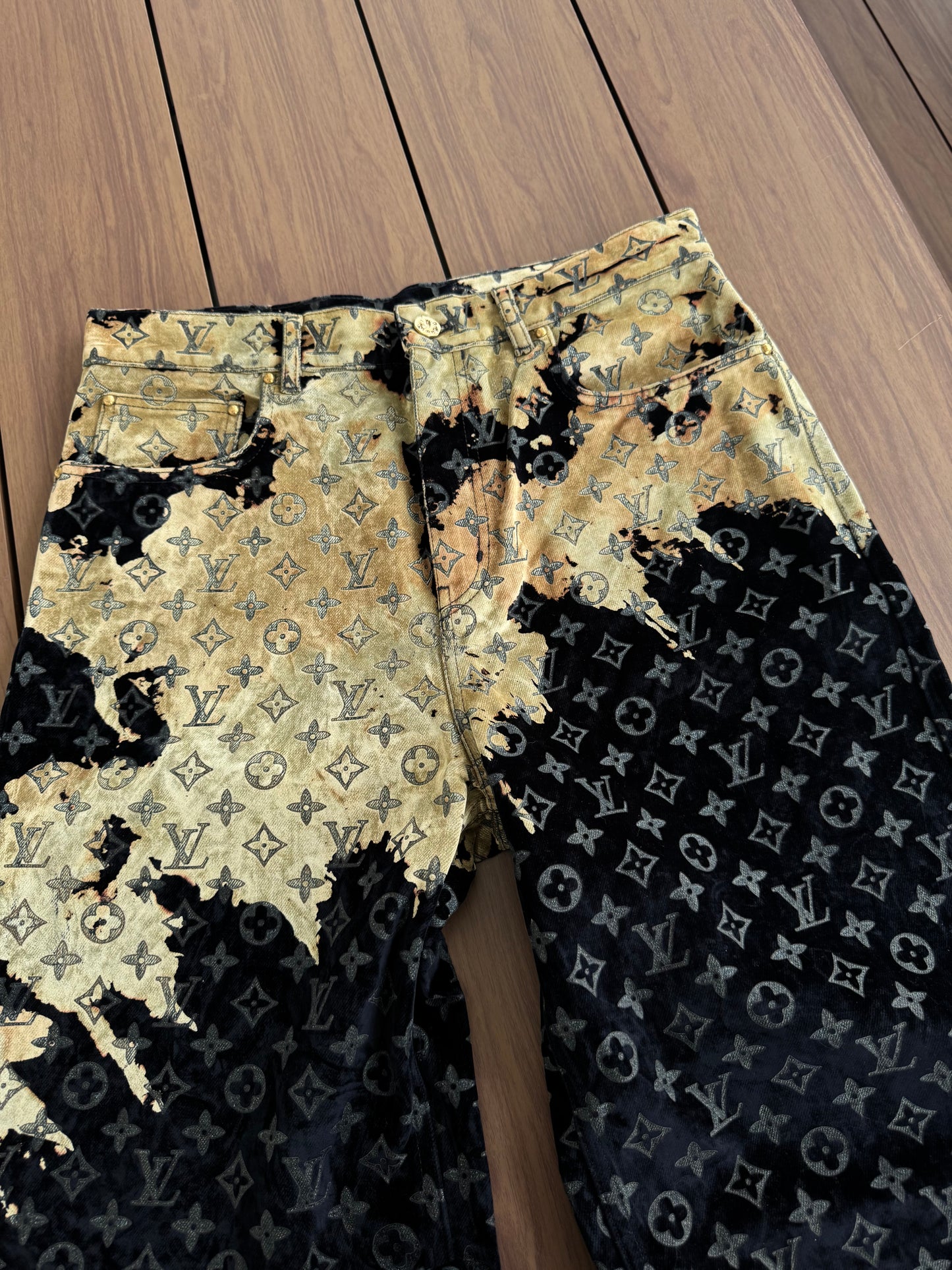 Louis Vuitton bleach monogram jeans close-up of gold bleach splatter wash detail over LV pattern on wood floor