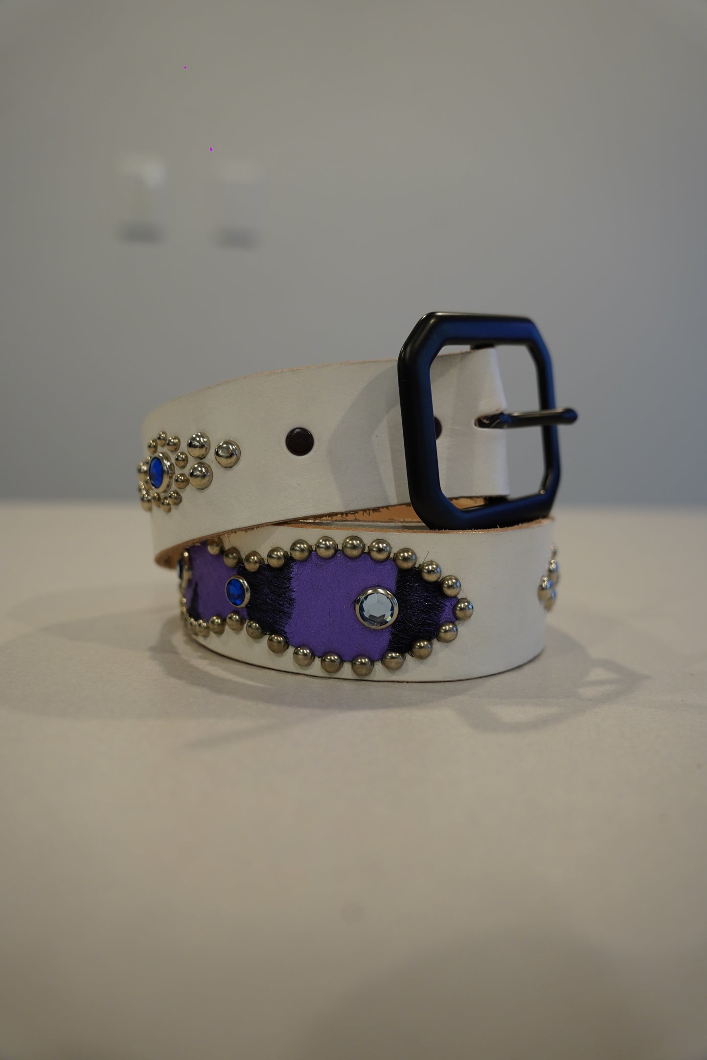 Vintage white leather belt coiled with purple ponyhair inlays, silver studs, blue rhinestones and black square buckle