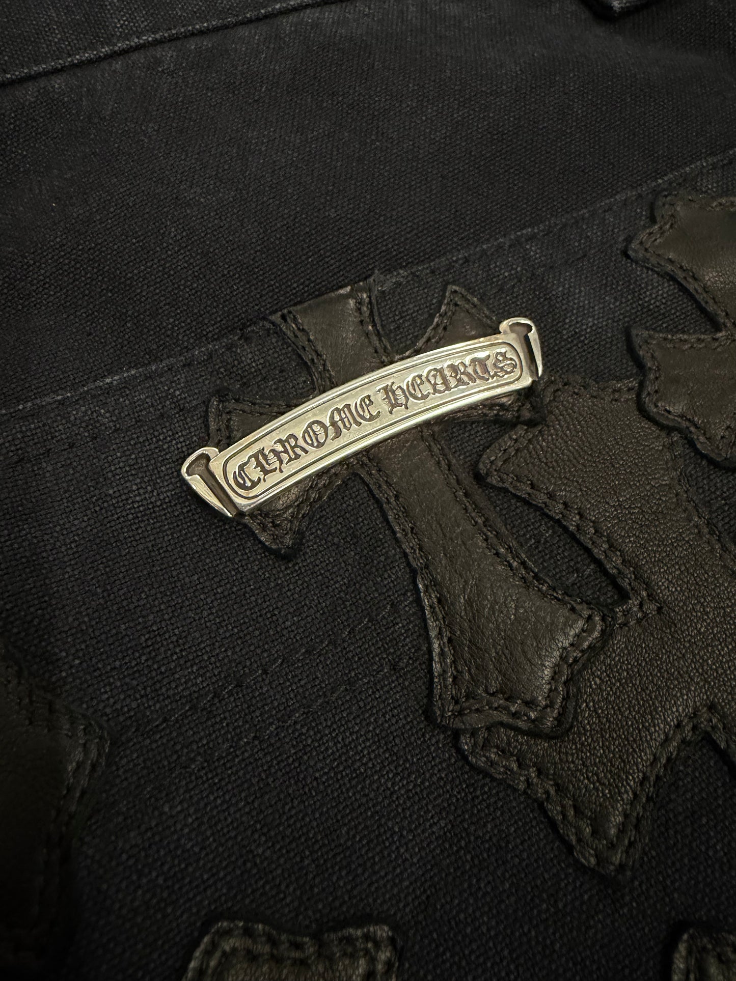 Chrome Hearts carpenter shorts macro view of silver Chrome Hearts scroll plaque among black leather cross patches