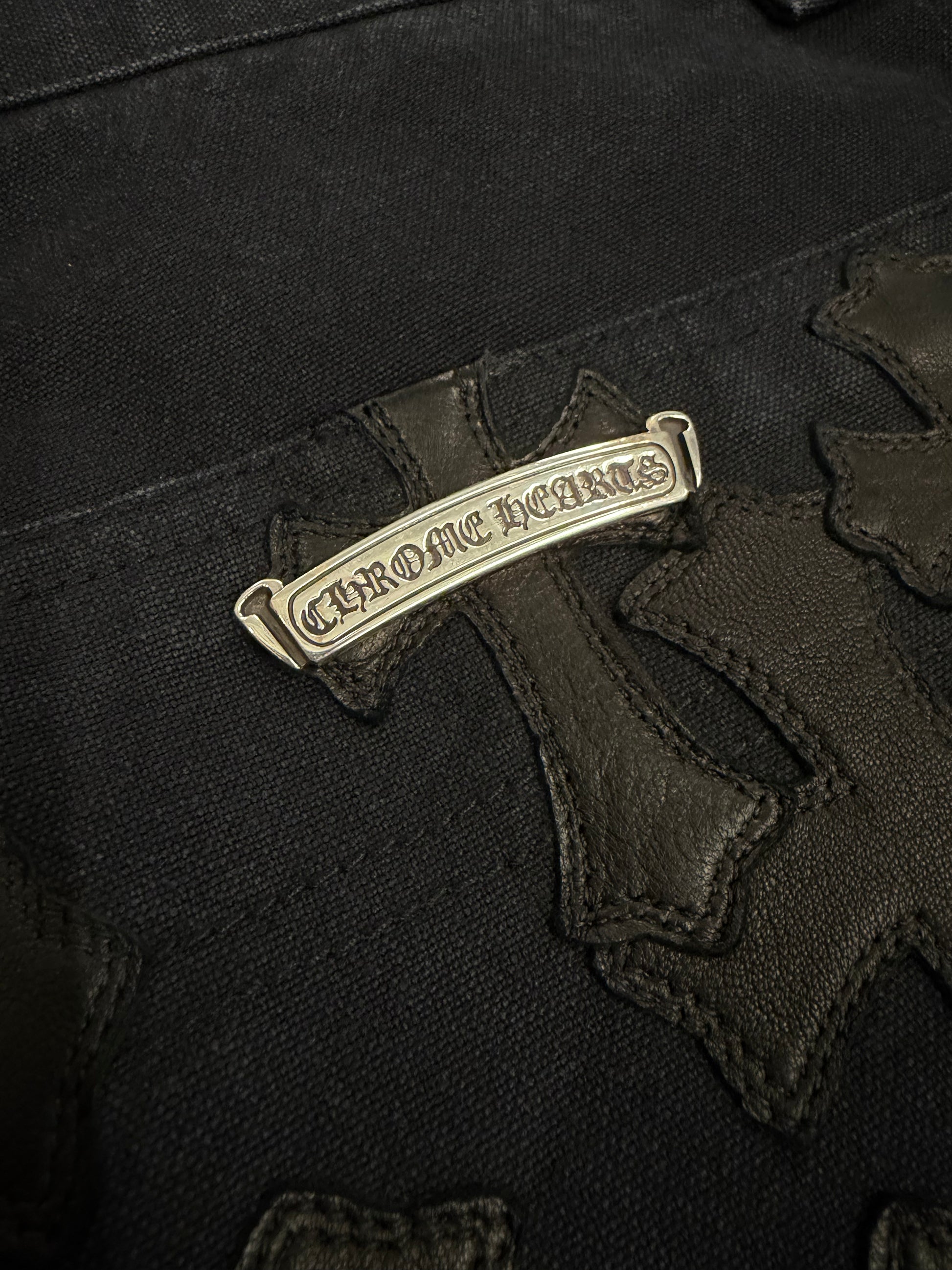 Chrome Hearts carpenter shorts macro view of silver Chrome Hearts scroll plaque among black leather cross patches