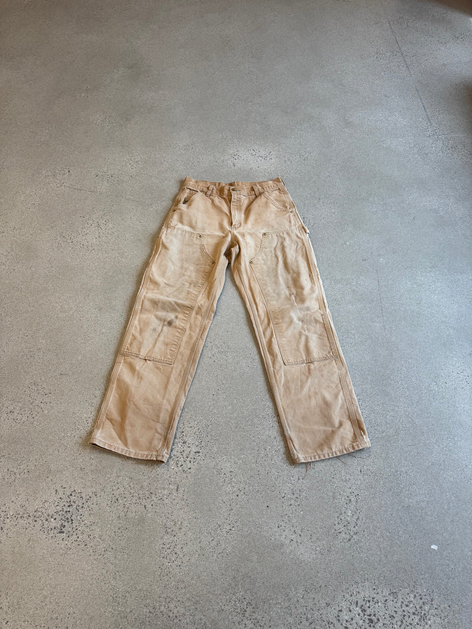 Vintage Carhartt tan double-knee carpenter pants in faded duck canvas with reinforced knee panels and utility loops.