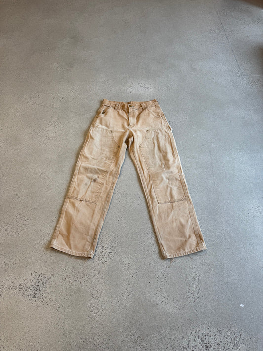 Vintage Carhartt tan double-knee carpenter pants in faded duck canvas with reinforced knee panels and utility loops.