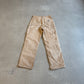 Vintage Carhartt tan carpenter pants back view with twin patch pockets and signature label, photographed on concrete.